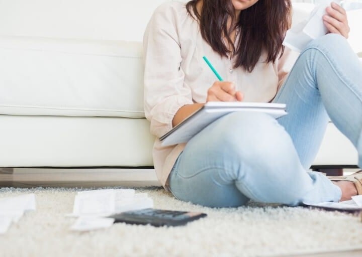 woman in jeans on floor, writing in notepad with a calculator
