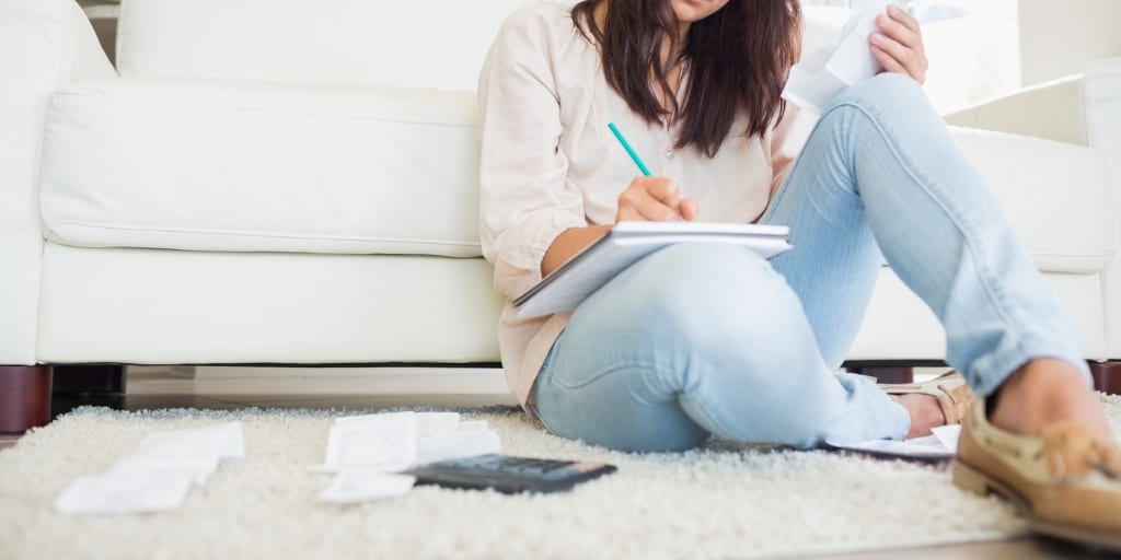 woman in jeans on floor, writing in notepad with a calculator