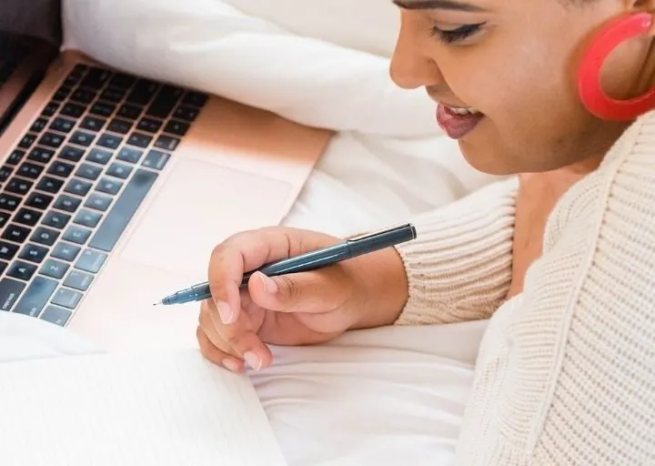 woman with big red earring, smiling, working on figuring out the purpose of her money by journaling