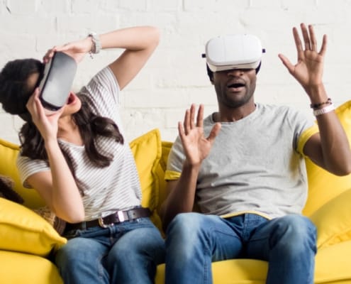 couple sitting on yellow sofa, with virtual gear over their eyes