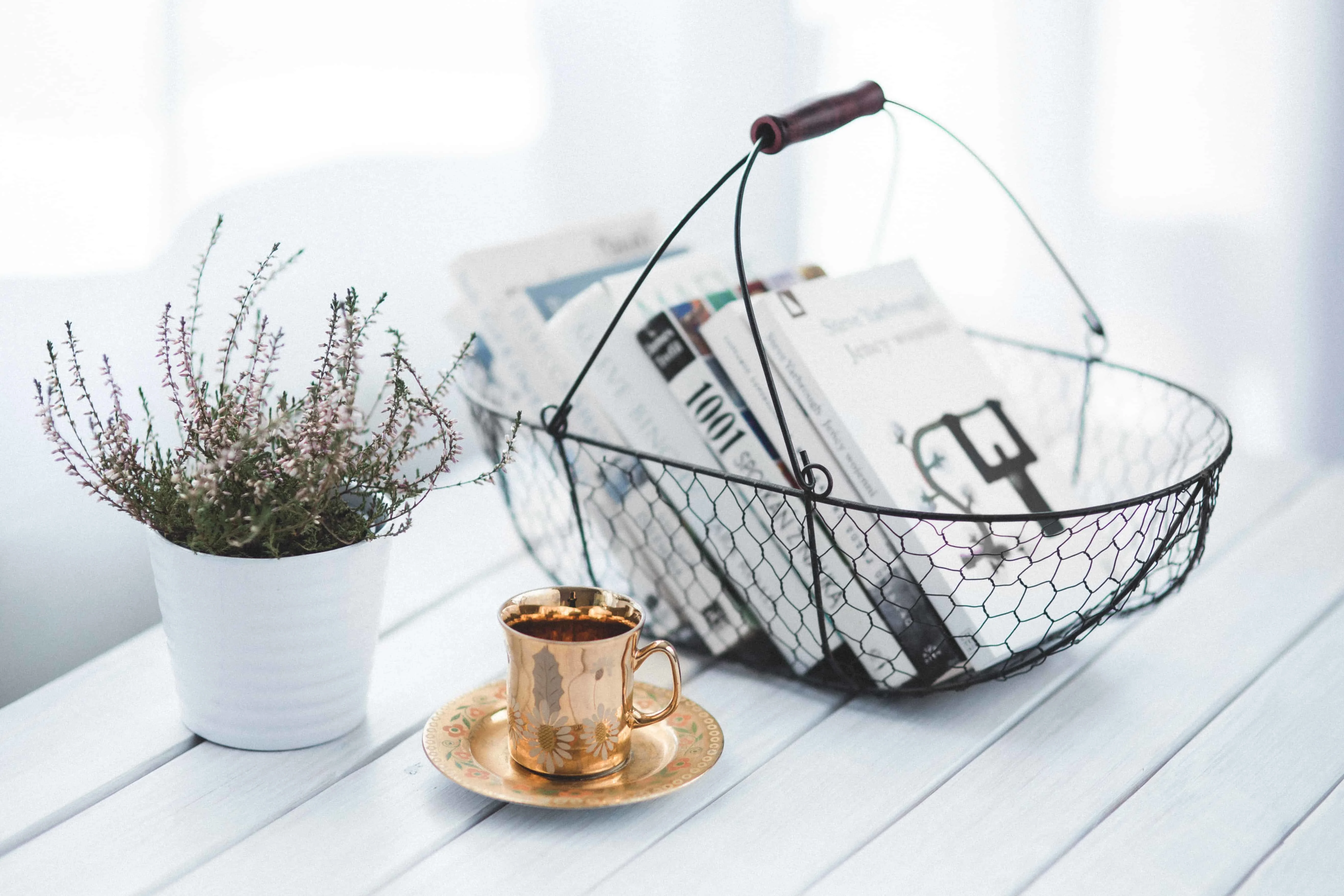 a basket with books, a copper coffee mug and plant on white table