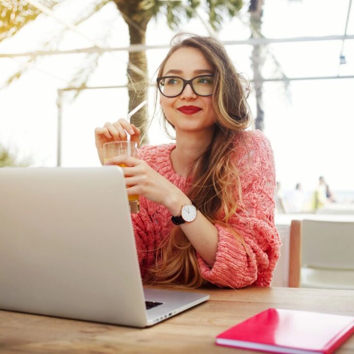 woman looking smartly in glasses, red lipstick, coffee drink, and laptop