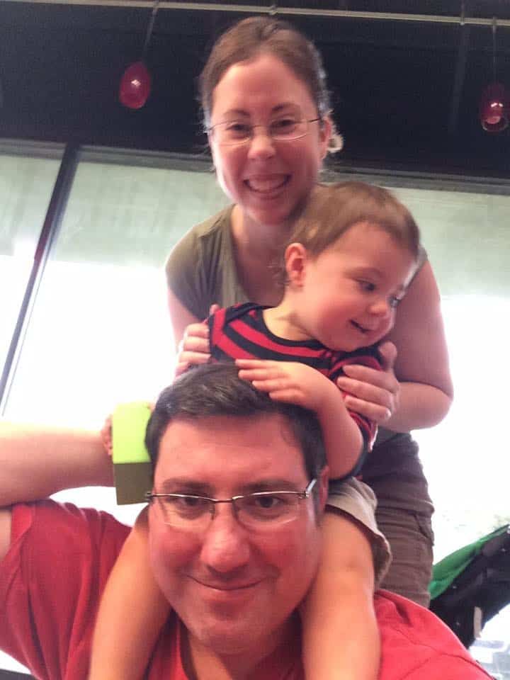 Photo of Amanda (author), and husband holding baby on his shoulders