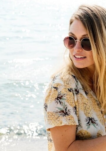 blonde woman looking over her shoulder at beach with iPhone