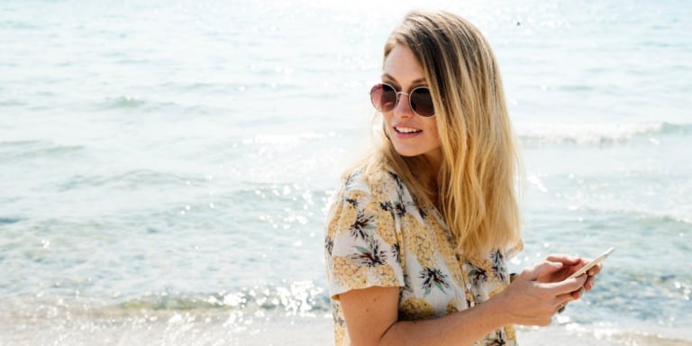 blonde woman looking over her shoulder at beach with iPhone