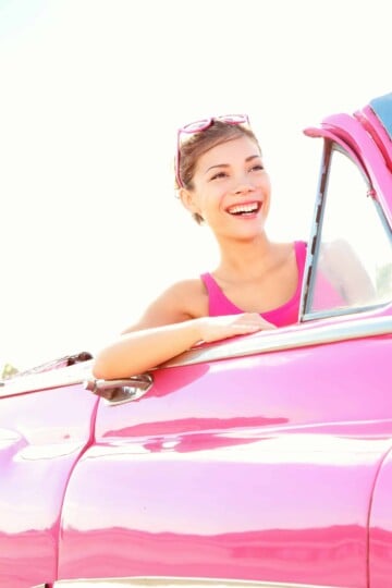 woman smiling driving a vintage pink cabriolet car