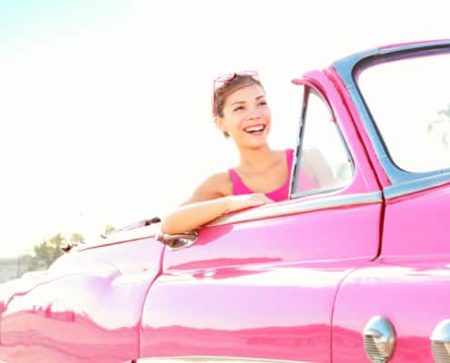 woman smiling driving a vintage pink cabriolet car