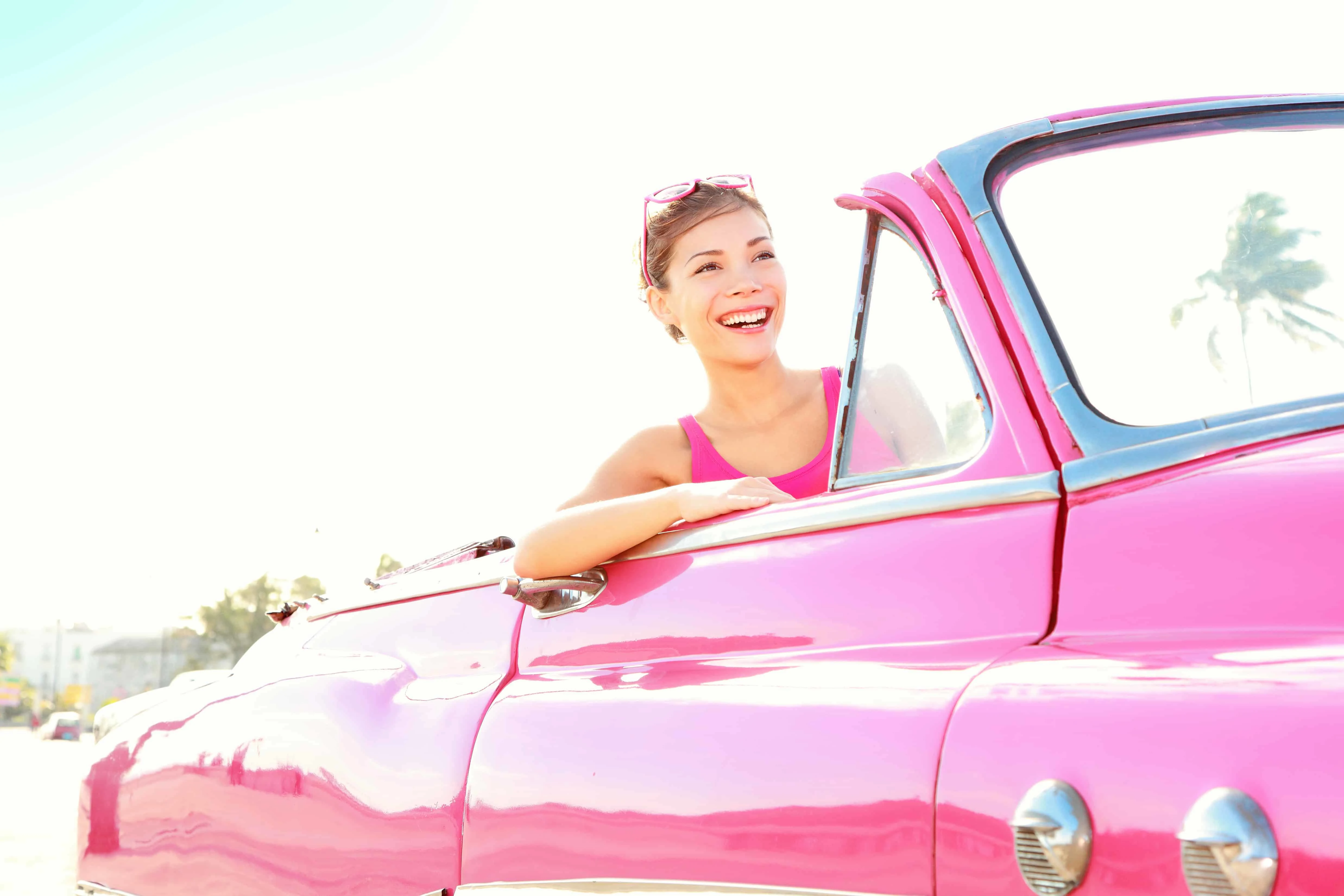 woman smiling driving a vintage pink cabriolet car