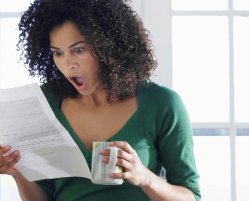 woman looking shocked at unexpected expenses (bill in hand)