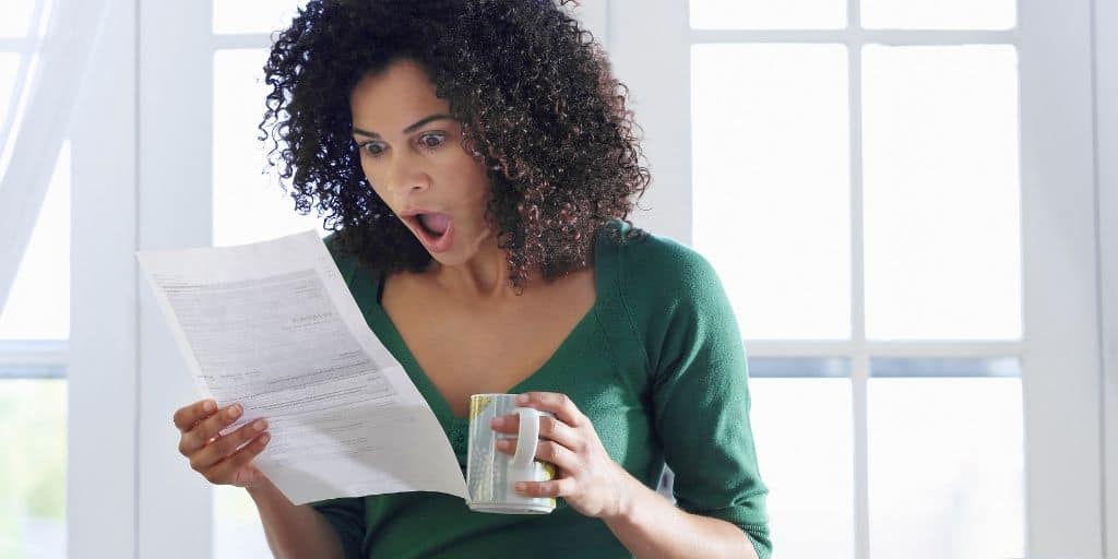 woman looking shocked at unexpected expenses (bill in hand)