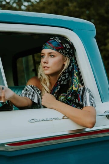 bohemian woman in blue and white truck, looking at herself in side view mirror