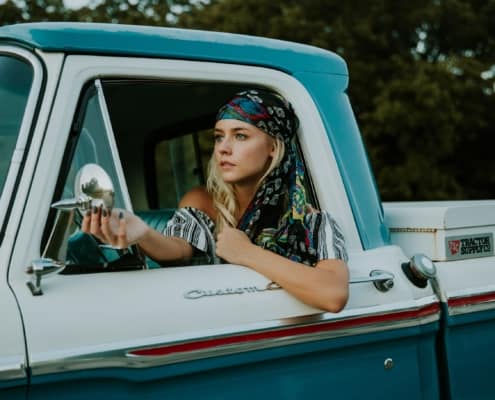 bohemian woman in blue and white truck, looking at herself in side view mirror