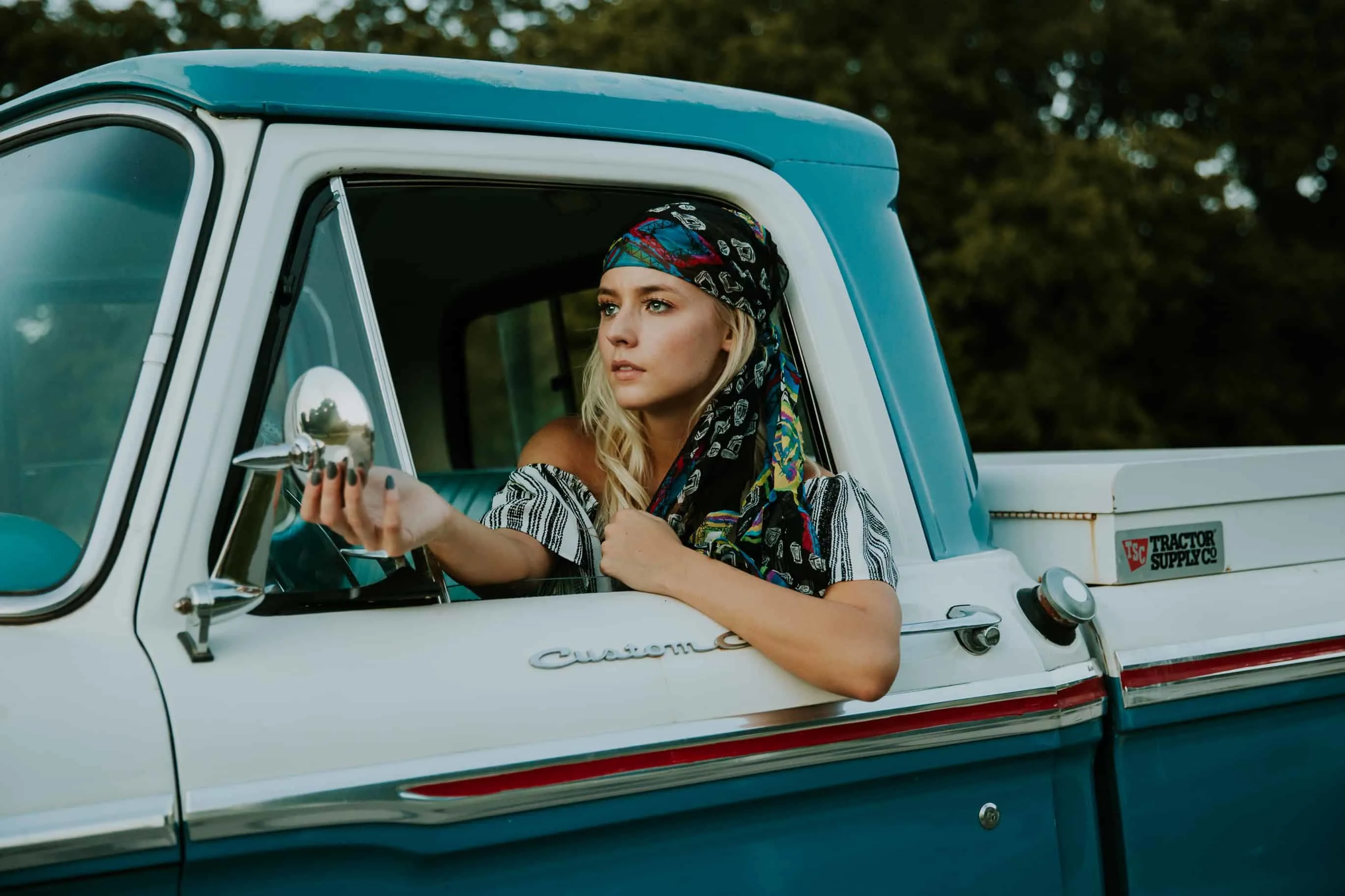bohemian woman in blue and white truck, looking at herself in side view mirror