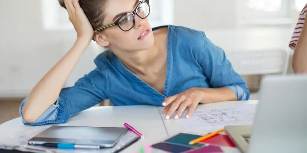 woman with glasses at desk, looking worried and wondering how to stop spending money on unnecessary things