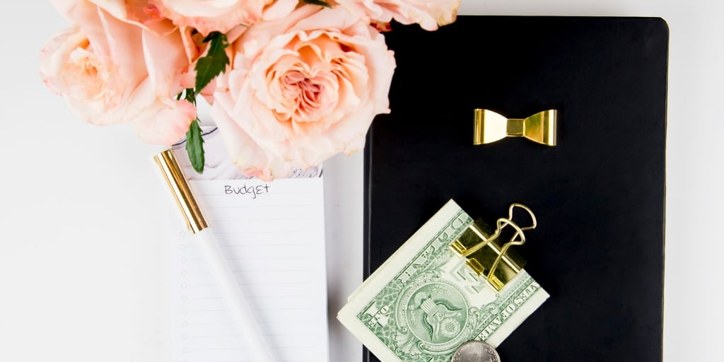 desktop with pink flowers, money in a clip, notepad and pen