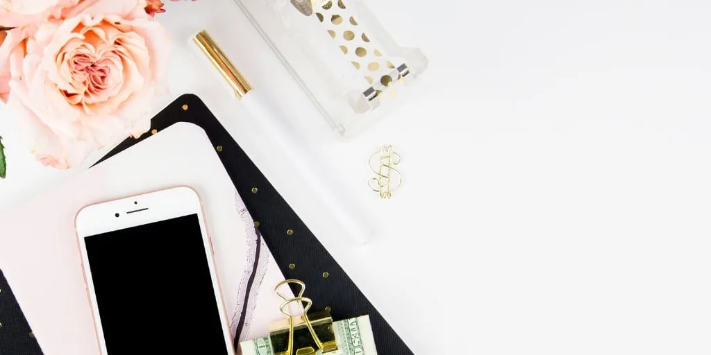 white desktop with flowers, money in clip and phone