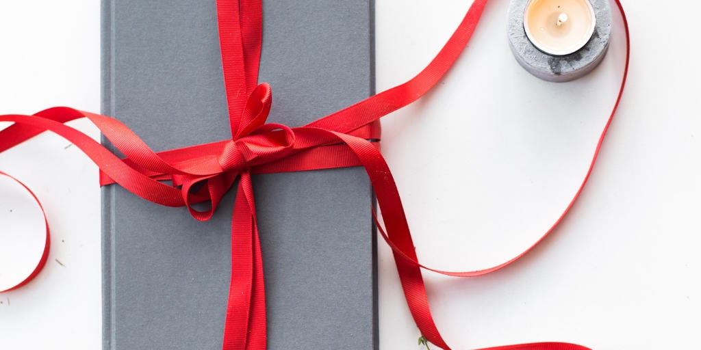 homemade holiday gift wrapped in a grey box with a red ribbon on a desk