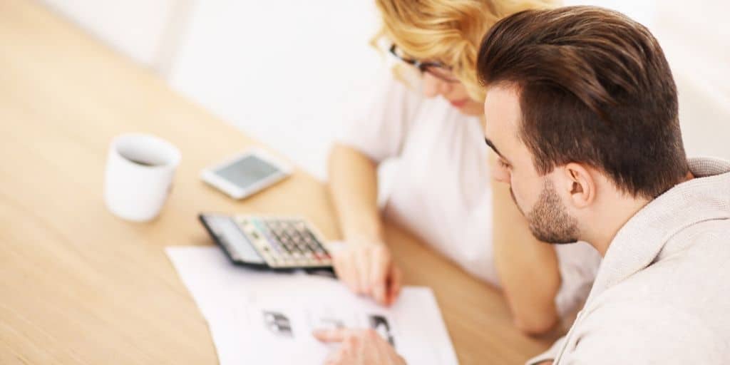 couple looking at finances with calculator on desk, figuring out how to drastically cut household expenses