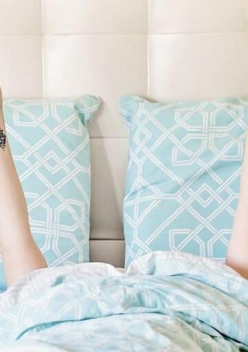 unemployed woman in bed with coffee and doing a peace sign, thinking about surviving unemployment