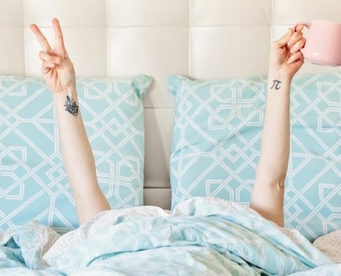 unemployed woman in bed with coffee and doing a peace sign, thinking about surviving unemployment