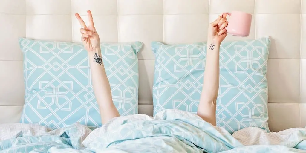 unemployed woman in bed with coffee and doing a peace sign, thinking about surviving unemployment
