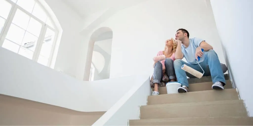 young couple sitting on stairs of new home, feeling house poor
