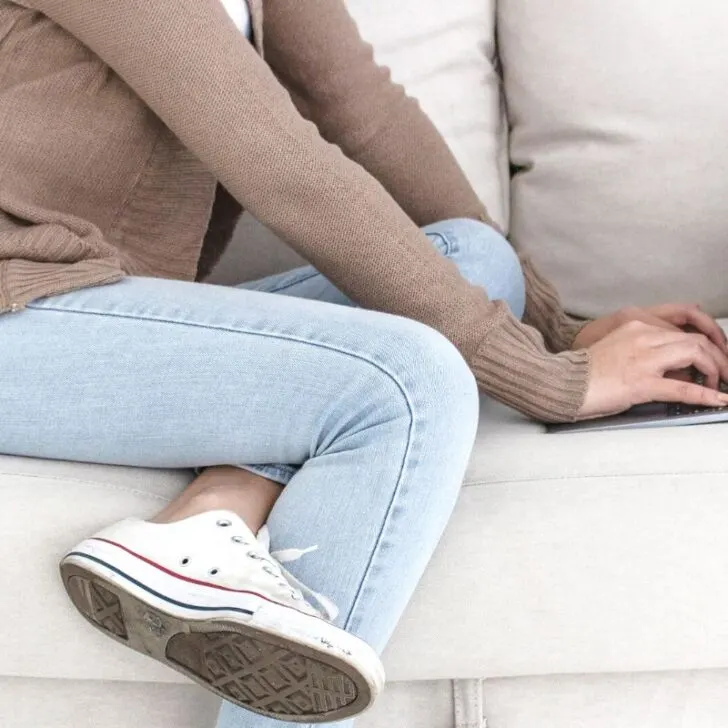 woman in sneakers on white couch, typing on computer