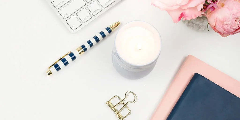 desktop with keyboard, pink flowers, a candle, a pen