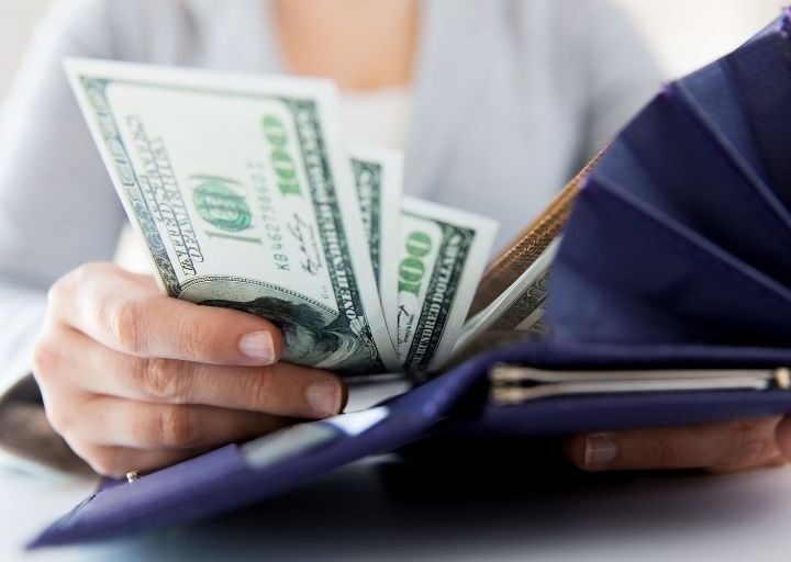 woman putting lots of saved money from money saving tips into navy blue wallet