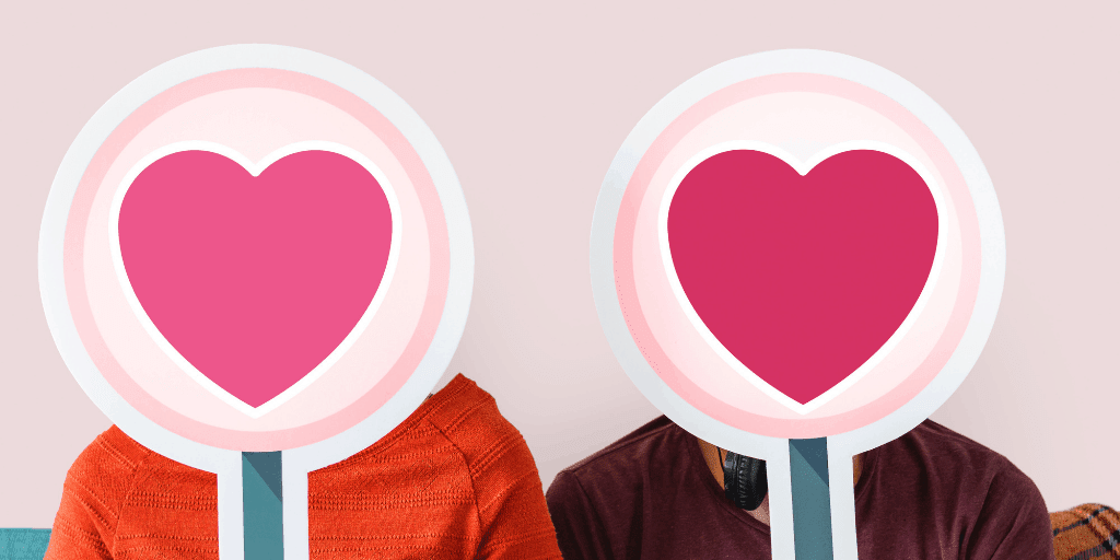 a couple sitting with two signs with hearts on them masking their faces