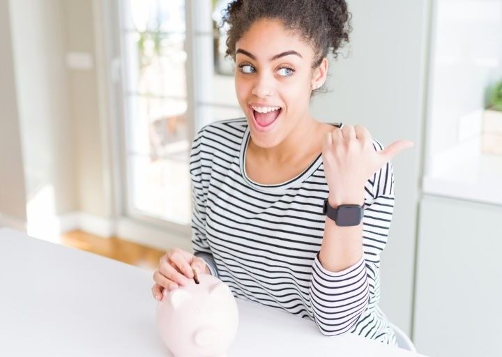 young woman with piggy bank, pointing and looking and smiling about importance of saving money for the future