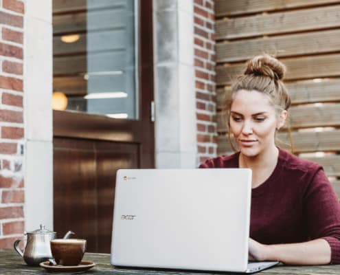 woman sitting outdoors at computer with brick wall background