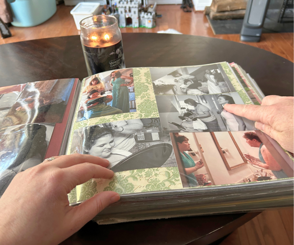 couple pointing at photos in wedding album on coffee table with candle light in background
