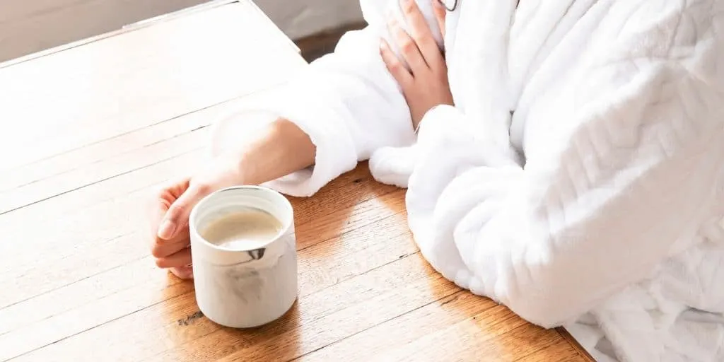 woman in robe at home with coffee mug, wondering can furloughed employees file for unemployment