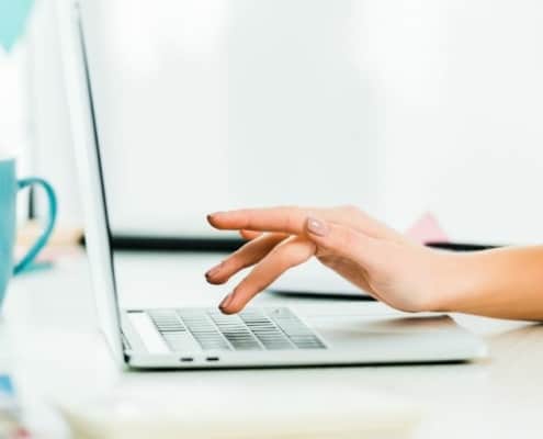 image of woman's hand working on laptop, with turquoise mug