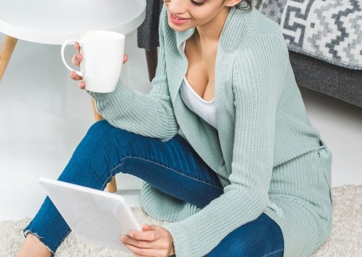 young woman on floor with coffee and laptop, smiling, reading about how to keep motivated to save money
