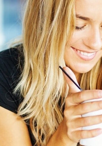 blonde woman looking down at coffee at hand, laughing about money life lessons she's learned