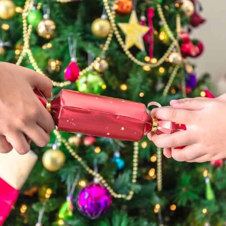 two people pulling apart a cracker tube in front of Christmas tree