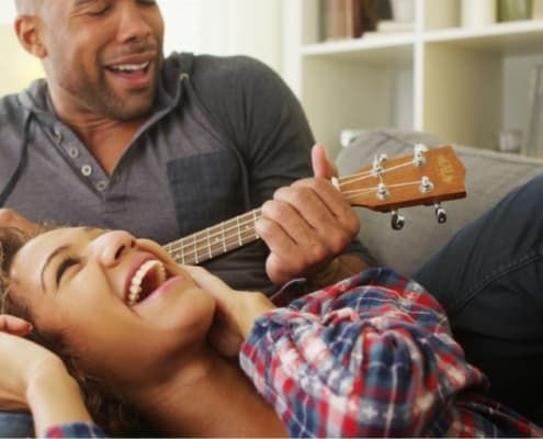 couple on couch, man playing ukele as part of list of cute couple things to do