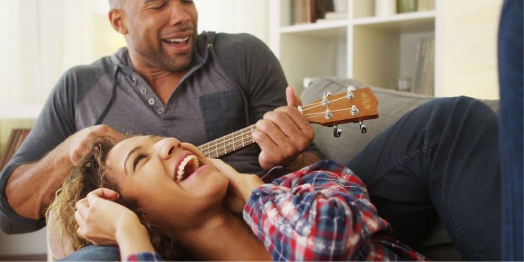 couple on couch, man playing ukele as part of list of cute couple things to do