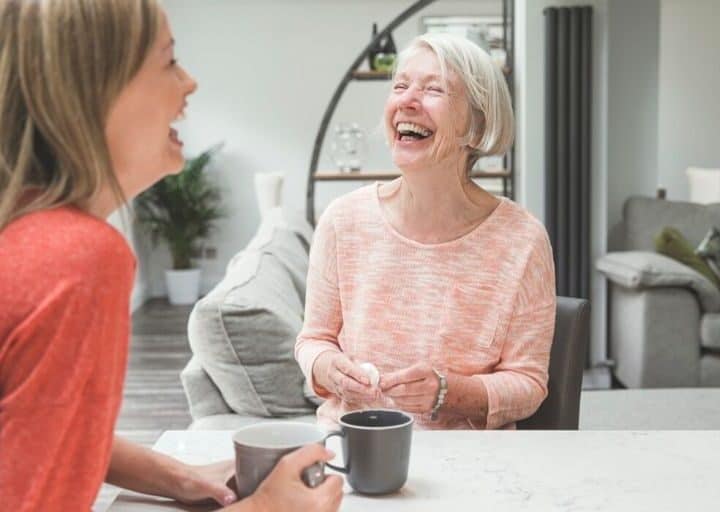 adult daughter and mother laughing together over tea