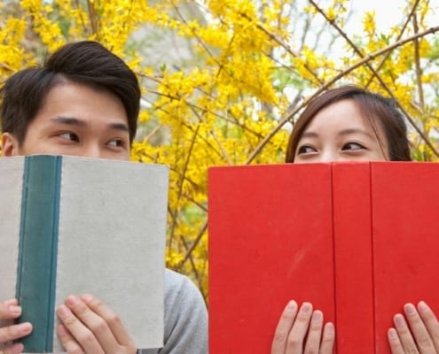 couple sitting on park bench behind books, flirting with each other - park date ideas