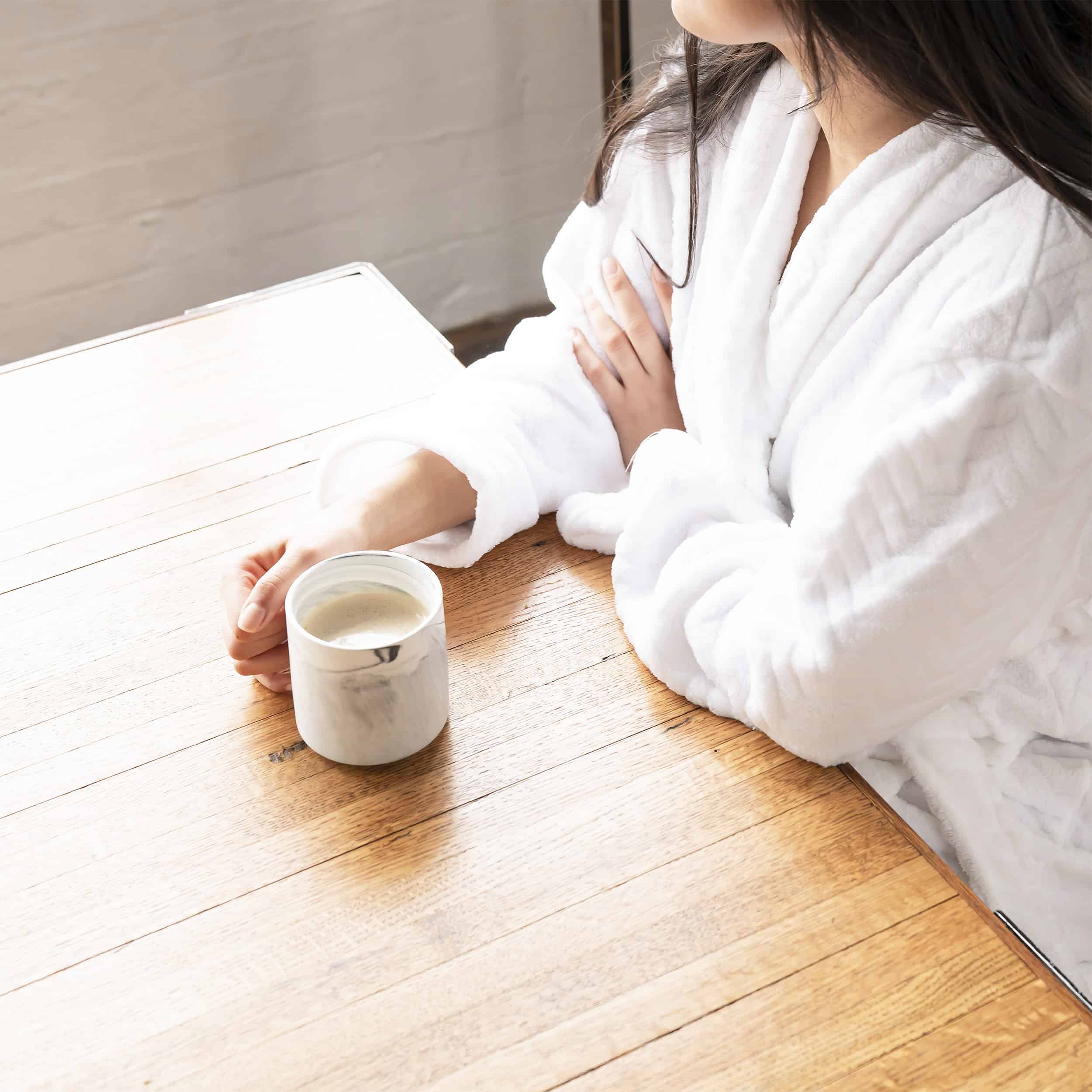 Woman sitting by window with cup of coffee, thinking about financial implications of divorce and whether or not to get a life insurance policy on her ex-spouse