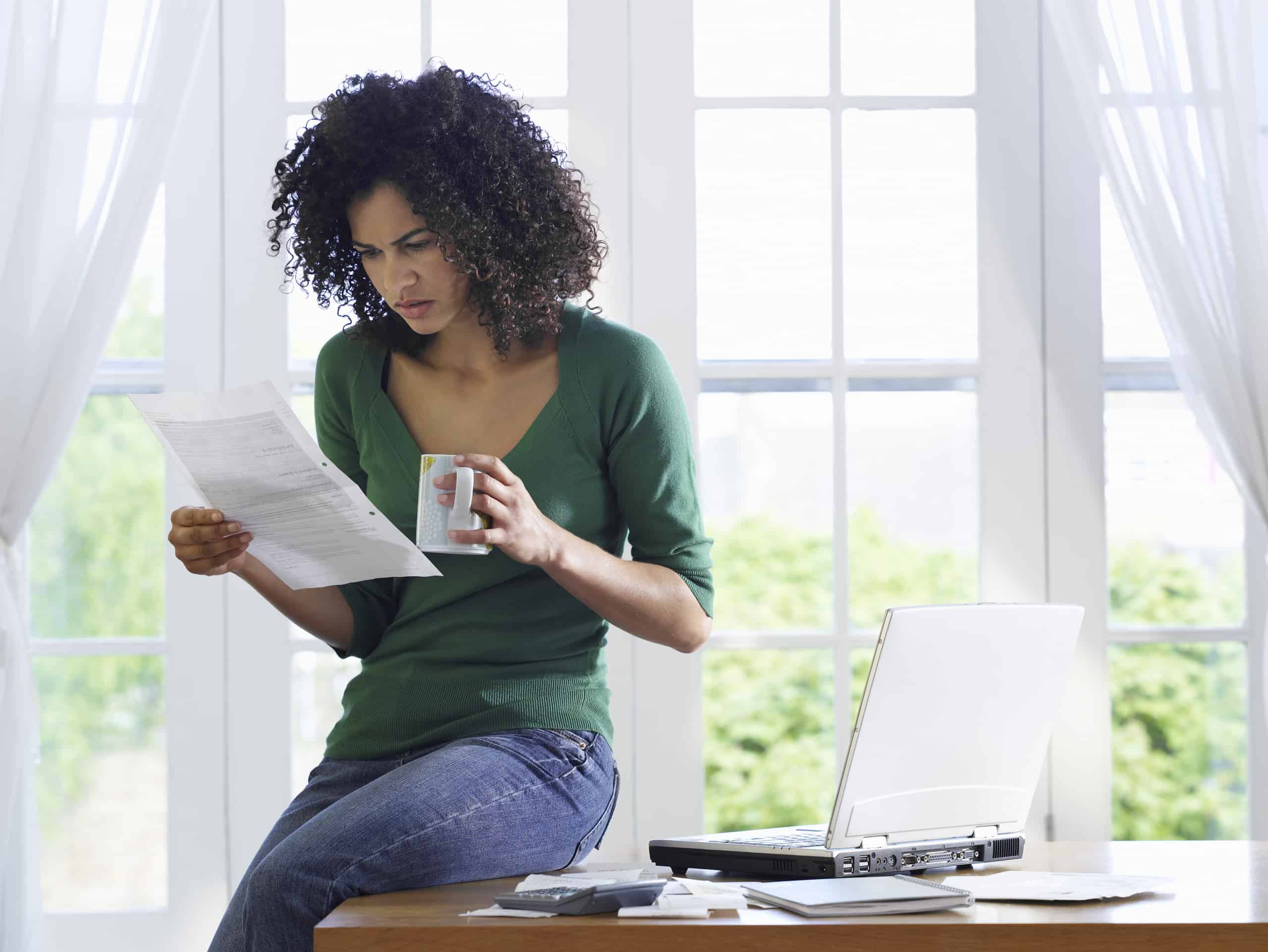 young woman with coffee mug, looking concerned at a piece of paper - wondering if someone has taken a life insurance policy out on her