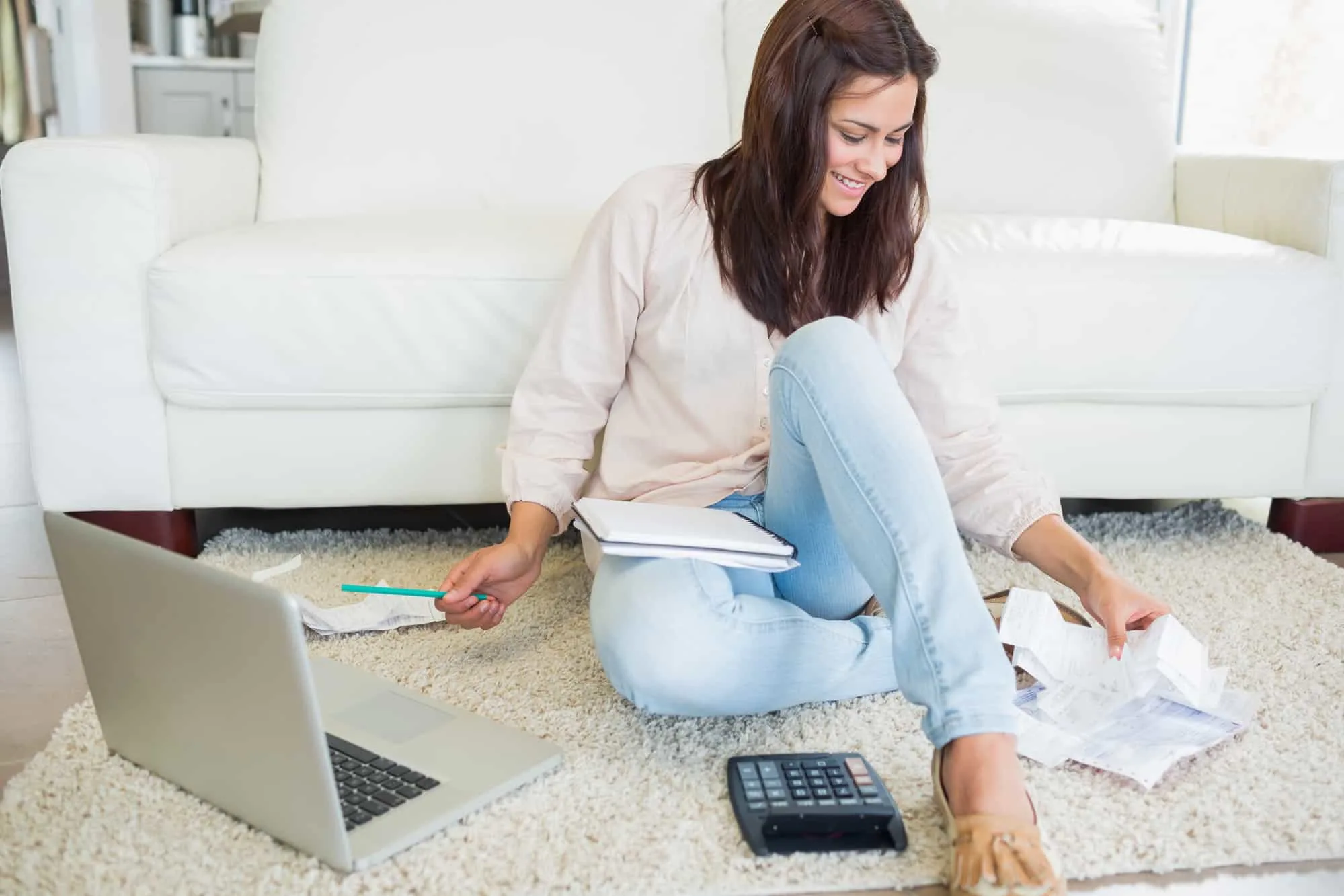 young woman sitting on carpet with bills and laptop, figuring out how to lower electric bill in apartment