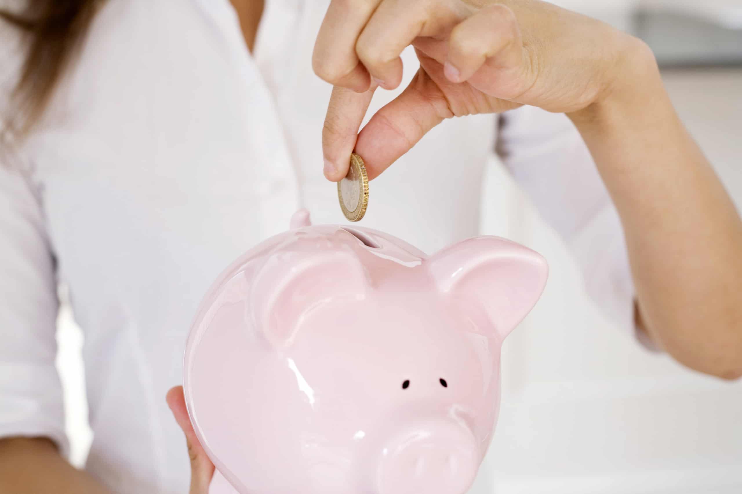 woman putting coins into piggy bank, thinking about how to save on electric bill in apartment