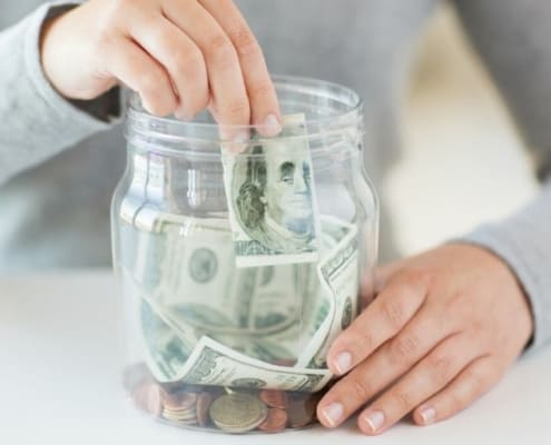 woman putting money into a money jar, wondering about money jar ideas she can use