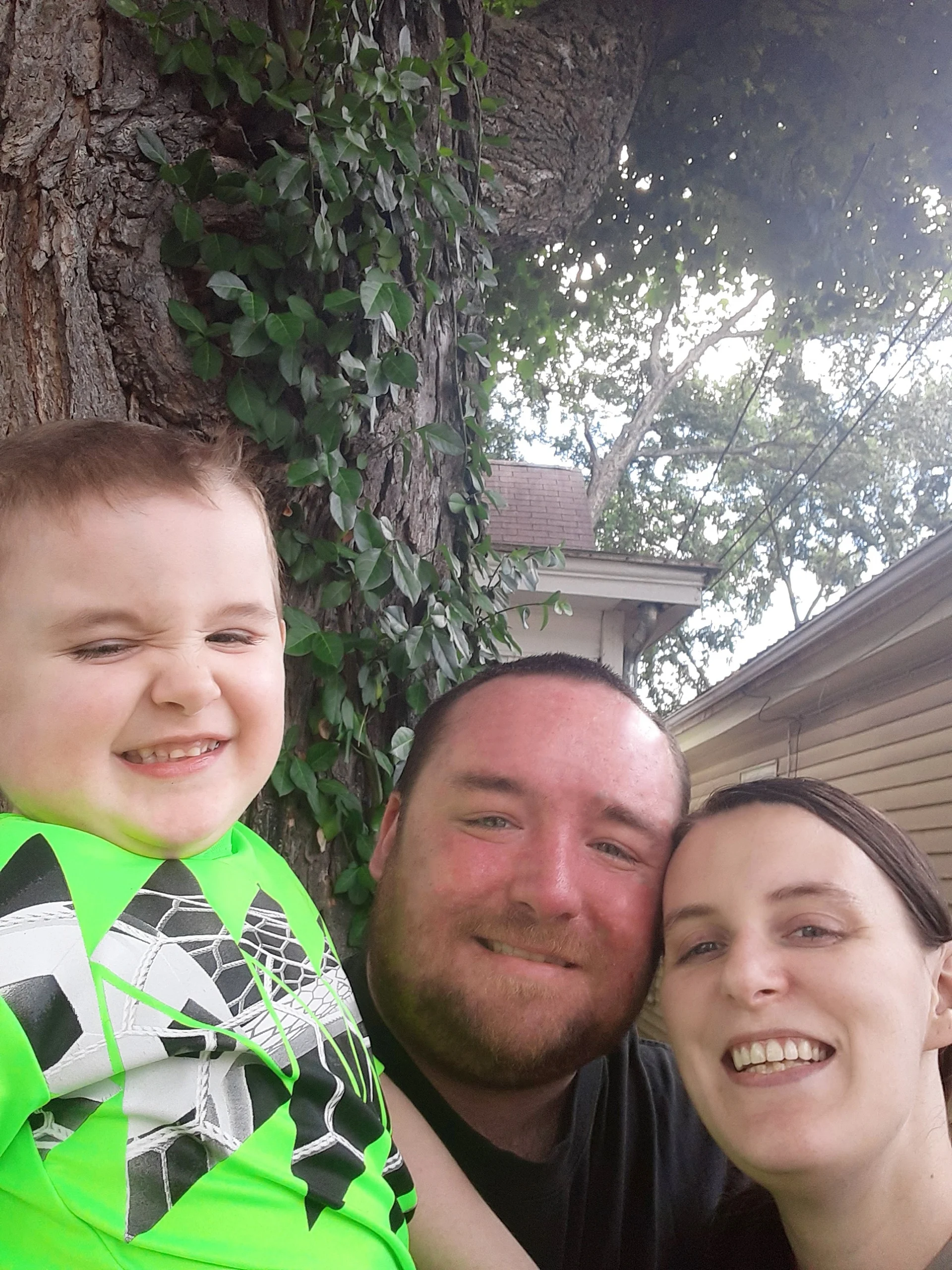 picture of Brittany and her husband and son in front of tree