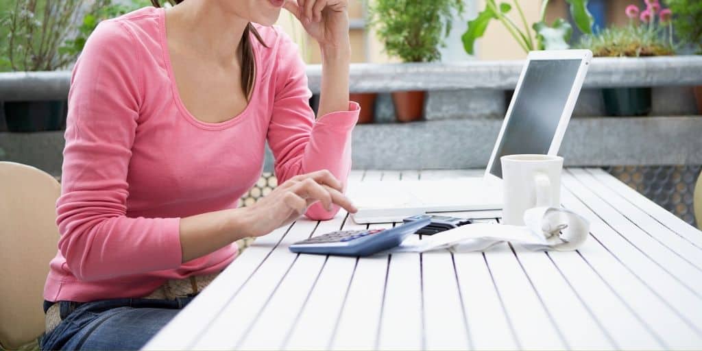 woman in pink shirt sitting in front of laptop with calculator, tired of living paycheck to paycheck