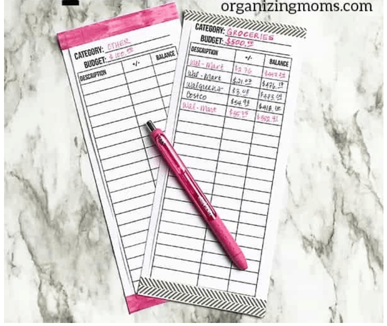 two vertical spending trackers the size of envelopes partly filled out, on marble background